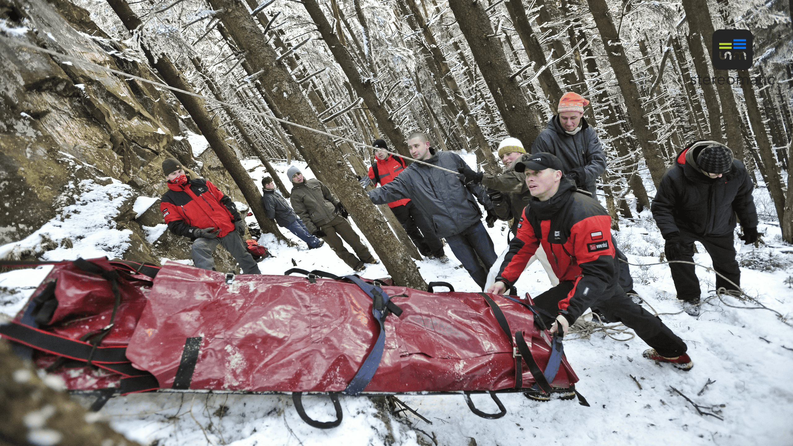 Symulacja akcji ratunkowej podczas firmowych warsztatów CSR w górach – uczestnicy transportują „poszkodowanego” na noszach w trudnym, zimowym terenie.
