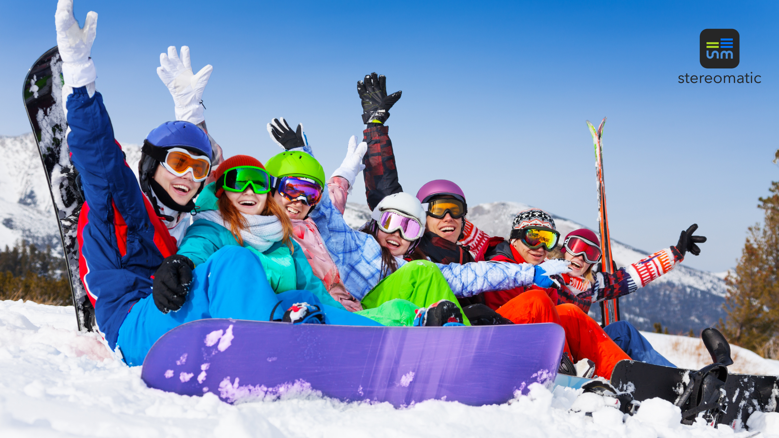 Grupa pracowników w kolorowych strojach zimowych, siedząca na śniegu z deskami snowboardowymi – zima, radość i team building w górach.