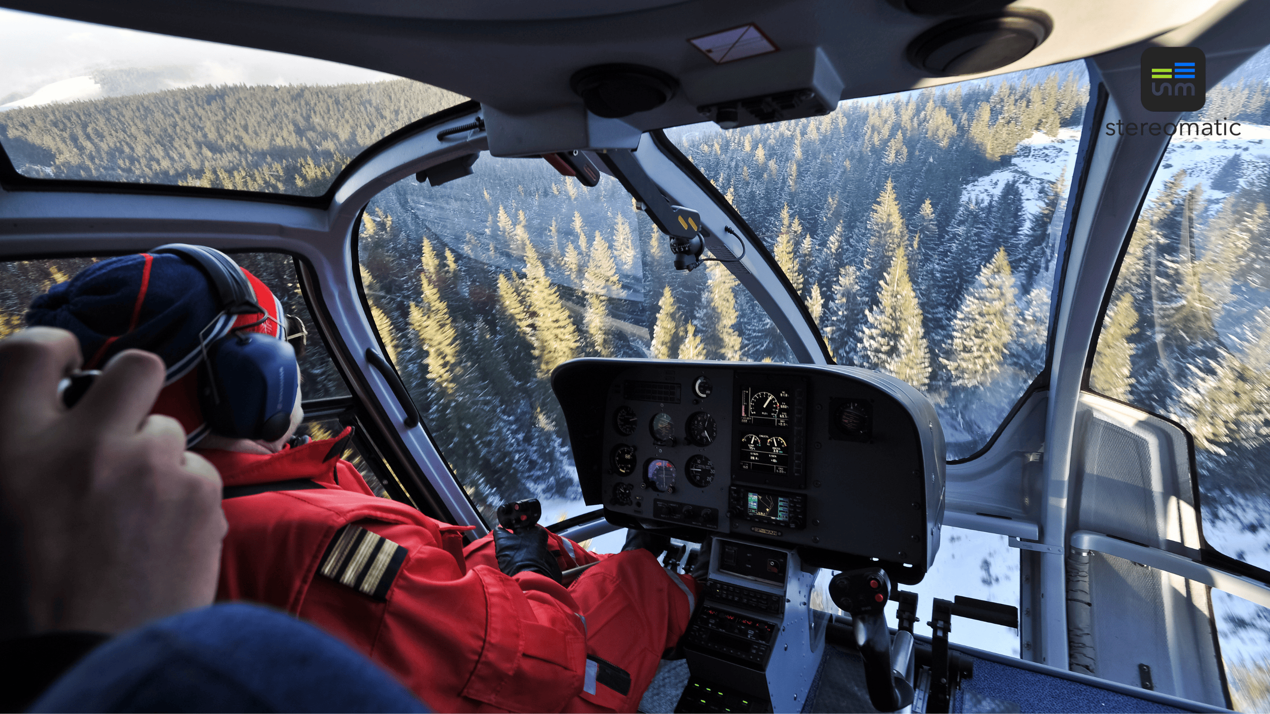 Widok z kabiny śmigłowca lecącego nad zaśnieżonymi górami – piloci w trakcie lotu integracyjnego podczas firmowego eventu.